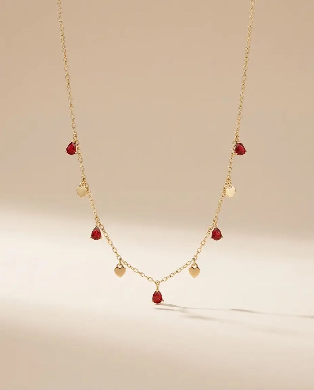Red crystal and gold heart station necklace in 925 sterling silver laid flat on a neutral background.