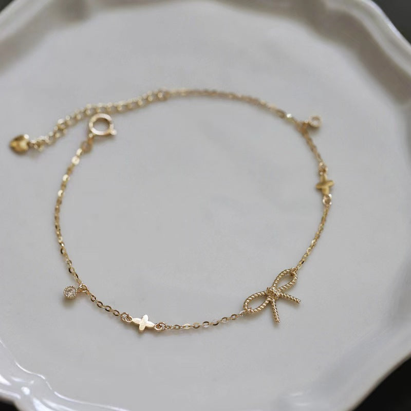 A delicate gold chain bracelet with small star and bow charms, displayed on a white ceramic dish.