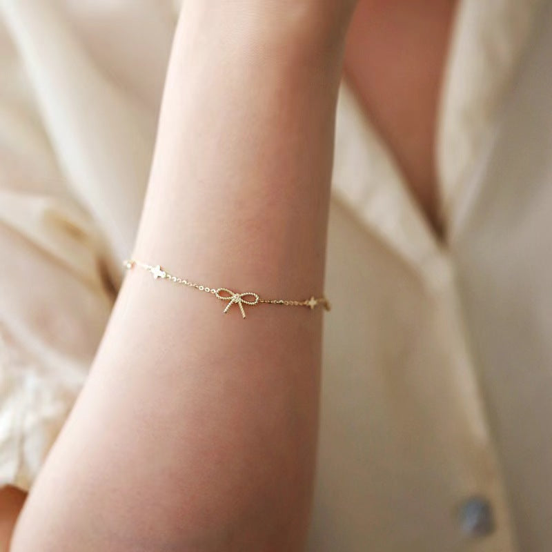 Gold bracelet with bow design on a wrist against a neutral background